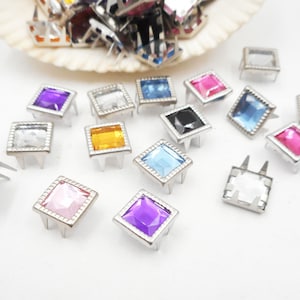 May include: Assortment of colorful square-shaped rhinestones with silver settings. The rhinestones are in various colors, including pink, blue, purple, and yellow.