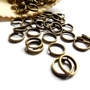 May include: A large pile of gold-colored jump rings, scattered on a white surface. The rings are small and round, with a smooth finish.