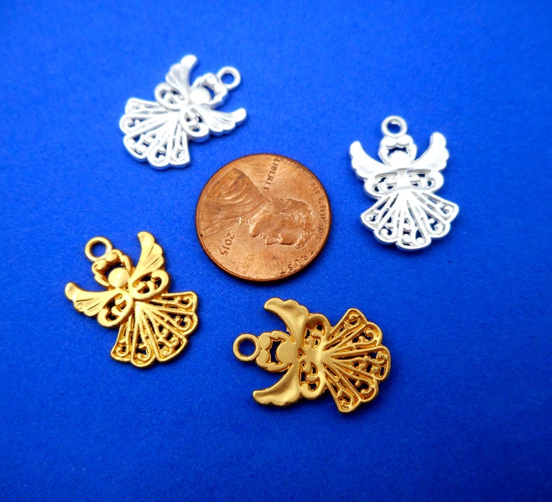 May include: Four angel charms, two gold and two silver, with intricate filigree designs. The charms are displayed on a blue background with a US penny for scale.