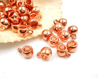 May include: A group of 20 rose gold metal bead caps with a loop on top. The bead caps are shiny and have a smooth finish.
