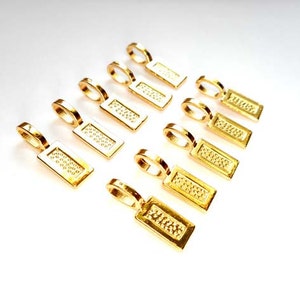 Puede incluir: Diez baúles de colgante de metal de color dorado con una superficie texturizada. Los baúles son de forma rectangular y tienen un pequeño bucle en la parte superior para sujetar una cadena o un cordón.