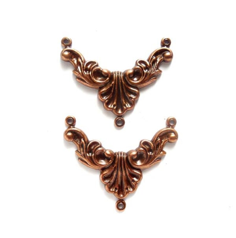 May include: Two ornate copper-colored metal embellishments with a decorative, floral design. Each piece has three holes for attaching to a project.