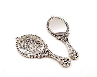 May include: Two ornate silver-toned hand mirrors with intricate floral designs. The mirrors are oval shaped and have a classic vintage style.
