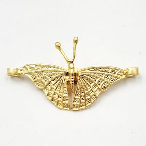 Puede incluir: Un objeto decorativo en forma de mariposa de color dorado. La mariposa tiene patrones de alas y antenas detallados. El objeto es probablemente un broche o un elemento decorativo para ropa o accesorios.