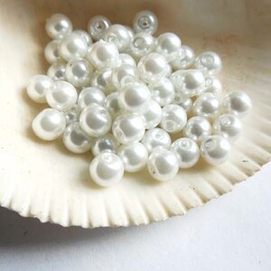 May include: A pile of white pearl beads in a seashell. The beads are round and smooth, and they are arranged in a random pattern.