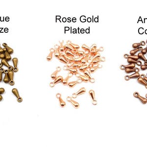 May include: Three piles of teardrop-shaped metal charms in antique bronze, rose gold plated, and antique copper finishes. Each pile contains approximately 40 charms.