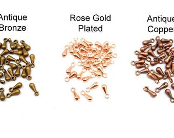 May include: Three piles of teardrop-shaped metal charms in antique bronze, rose gold plated, and antique copper finishes. Each pile contains approximately 40 charms.