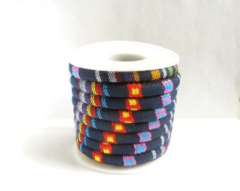 May include: A spool of navy blue rope with a colorful woven pattern. The pattern includes red, yellow, purple, and blue squares. The rope is coiled on a white plastic spool.