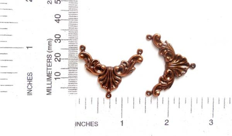 May include: Two antique copper-colored metal corner embellishments with a decorative floral design. Each piece has three holes for attaching to a project.
