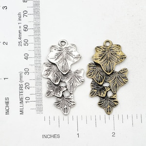May include: Two metal charms in the shape of ivy leaves. The charm on the left is silver and the charm on the right is gold. Both charms are approximately 2 inches long.