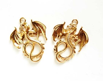 May include: Two gold-colored dragon charms with wings outstretched. The dragons are detailed with scales and have a loop at the top for attaching to jewelry or other crafts.