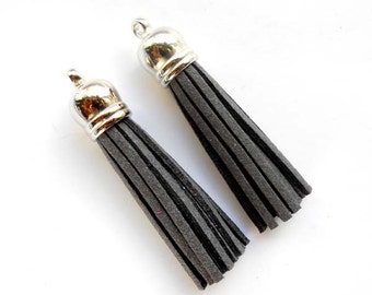 May include: Two gray suede tassels with silver metal tops. The tassels are about 3 inches long.