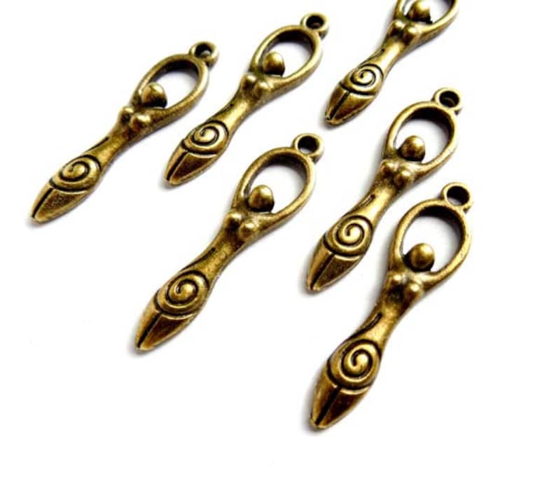 May include: Six antique gold-toned metal charms featuring a stylized female figure with a spiral design. The charms have a loop at the top for attaching to jewelry or other crafts.