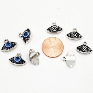 May include: A collection of silver-toned evil eye charms with blue and white enamel. The charms are in the shape of an eye and have a loop at the top for attaching to jewelry or other crafts.