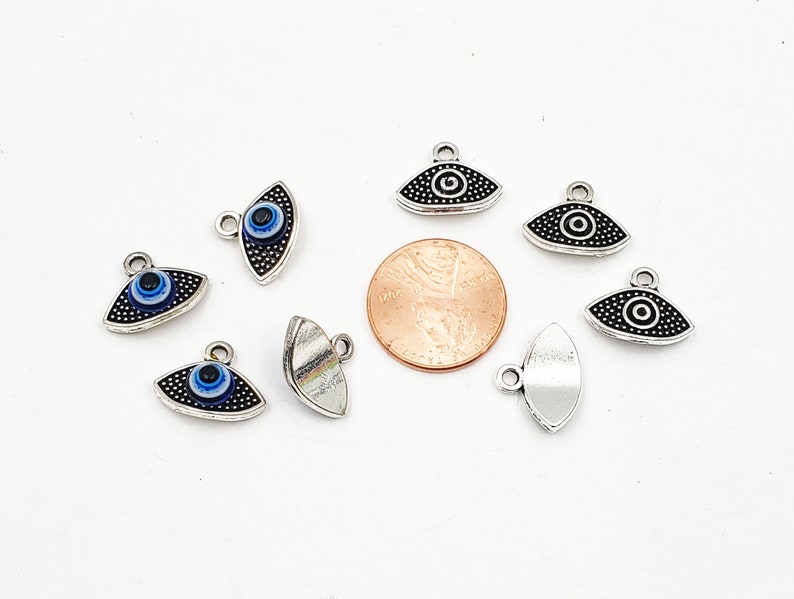 May include: A collection of silver-toned evil eye charms with blue and white enamel. The charms are in the shape of an eye and have a loop at the top for attaching to jewelry or other crafts.