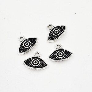 May include: Four silver charm pendants with a black evil eye design. Each pendant has a small loop at the top for attaching to a chain or bracelet.