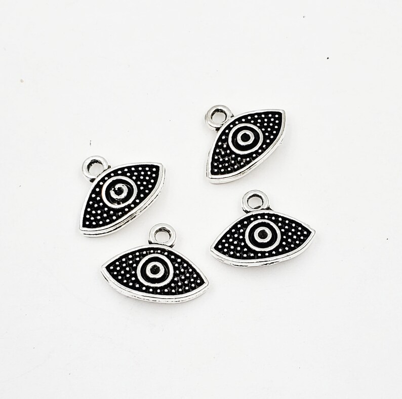 May include: Four silver charm pendants with a black evil eye design. Each pendant has a small loop at the top for attaching to a chain or bracelet.
