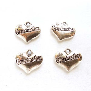 Op de afbeelding: Vier zilverkleurige hartvormige bedels. Elke bedel heeft het woord "Grandmother" in een scriptlettertype. Boven het woord is een kleine, heldere edelsteen geplaatst. Ideaal voor het maken van sieraden of knutselen.