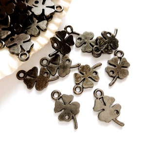 May include: A group of antique silver-toned four-leaf clover charms with a loop for attaching to jewelry or other crafts.
