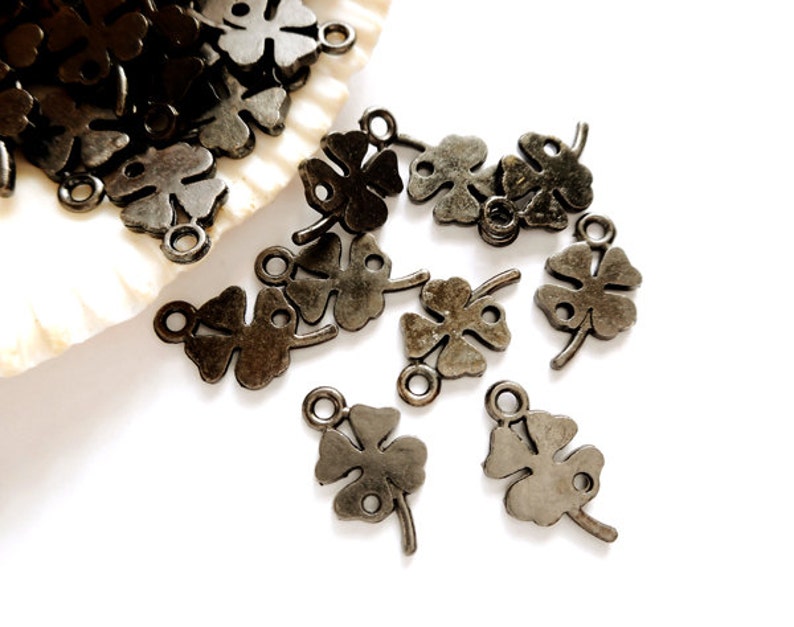 May include: A group of antique silver-toned four-leaf clover charms with a loop for attaching to jewelry or other crafts.