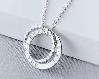 May include: A silver necklace featuring two interlocking rings. One ring is smooth with engraved text, while the other is textured with small beads. The necklace hangs on a delicate chain, perfect for everyday wear.