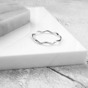 May include: A silver wavy ring on a white surface.