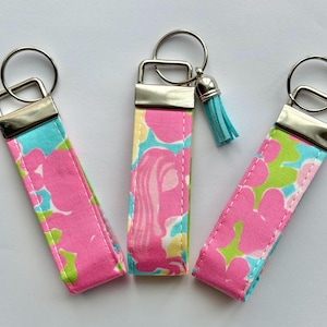 May include: Three fabric key fobs with silver-tone hardware. The key fobs feature a floral pattern in pink, green, and yellow on a turquoise background. One key fob has a small blue tassel.