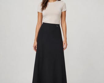 Può includere: Una t-shirt beige a maniche corte con girocollo abbinata a una gonna lunga nera a trapezio. La gonna presenta una vita alta con un piccolo e discreto dettaglio logo color argento vicino alla cintura e un tessuto liscio e fluido.