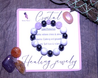 May include: A crystal healing bracelet with white, black, and lavender beads. The bracelet is on a pink card with the words "Crystal Healing jewelry". Additional crystals and a sage bundle are also present.