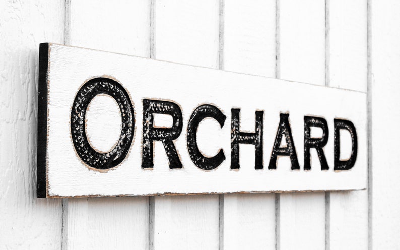May include: White wooden sign with black lettering that reads "ORCHARD".