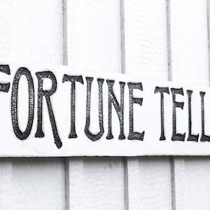 May include: White wooden sign with black lettering that reads "FORTUNE TELLER".