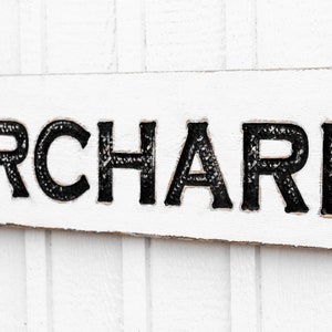 May include: White wooden sign with black lettering that reads "ORCHARD".
