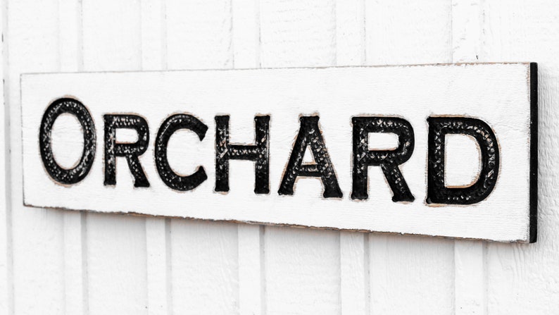 May include: White wooden sign with black lettering that reads "ORCHARD".