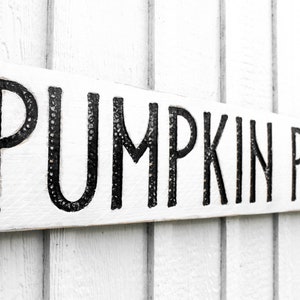 May include: White wooden sign with black lettering that reads "Pumpkin Patch".