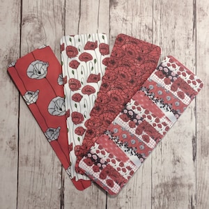 May include: Four different bookmark designs featuring red poppy flowers with black outlines. The bookmarks are printed on white paper and have a red, white, and black color scheme.