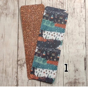 May include: Two bookmarks, one with a copper glitter finish and the other with a colorful pattern of plants and pots. The patterned bookmark has a dark blue background with orange, green, and white accents.