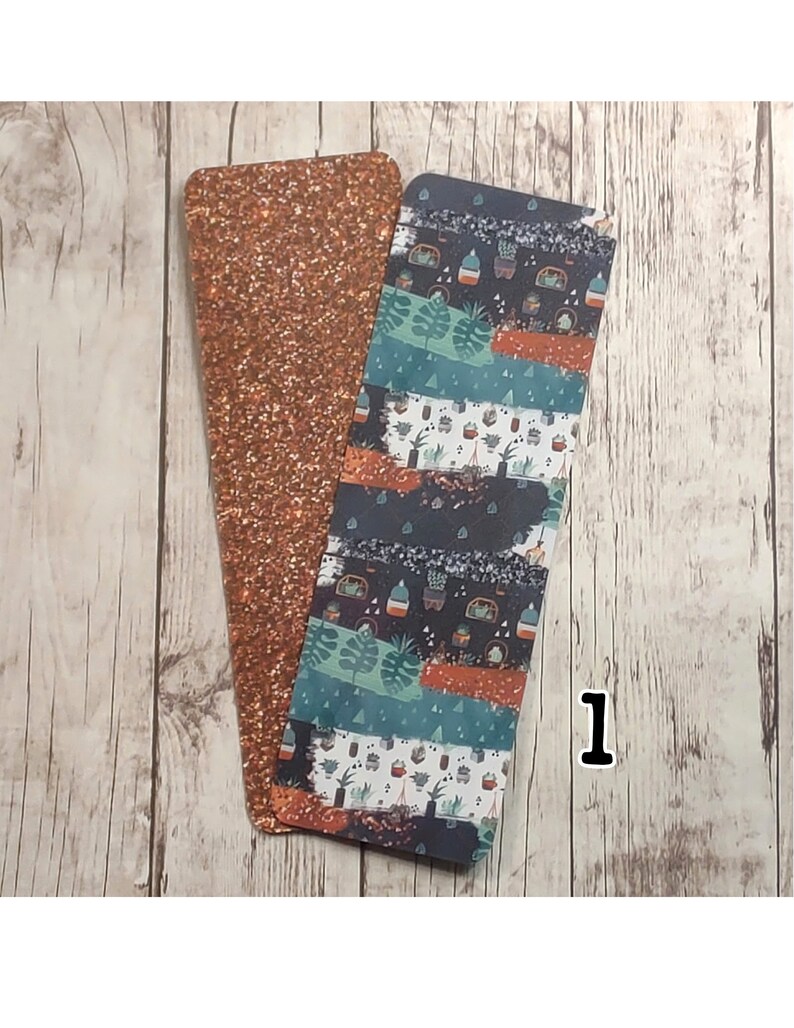 May include: Two bookmarks, one with a copper glitter finish and the other with a colorful pattern of plants and pots. The patterned bookmark has a dark blue background with orange, green, and white accents.