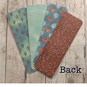 May include: Four different bookmark designs. One bookmark has a geometric pattern with copper accents on a blue background. Another bookmark has a green and white striped pattern. A third bookmark has a blue background with white leaves. The fourth bookmark has a copper glitter background. The back of the bookmarks is visible.