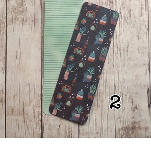 May include: Two bookmarks, one with a green and white striped pattern and the other with a black background and a repeating pattern of potted plants in various colors.