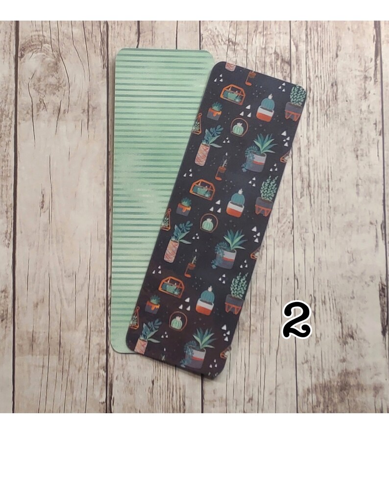 May include: Two bookmarks, one with a green and white striped pattern and the other with a black background and a repeating pattern of potted plants in various colors.