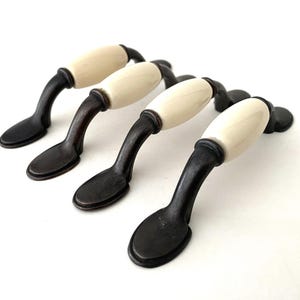 May include: Four black metal cabinet pulls with off-white ceramic knobs. The pulls are curved and have a rounded oval shape.