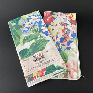 May include: Two folded Waverly Home Fashions napkins with floral patterns. One napkin features blue, green, and white flowers, while the other has red, yellow, and pink blooms. The napkins are labeled "Newstead Parrot" and are 17 x 17 inches.