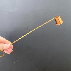 May include: A gold candle snuffer with a twisted handle and a round, cup-shaped end.