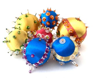 May include: A collection of six decorative Christmas ornaments. The ornaments are spherical, with a satin-like texture, and adorned with sequins, beads, and other embellishments in various colors, including yellow, blue, and red.