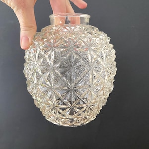May include: Clear glass globe-shaped lampshade with a detailed, geometric pattern. The shade has a round shape with a small opening at the top. The glass is transparent, allowing light to pass through.