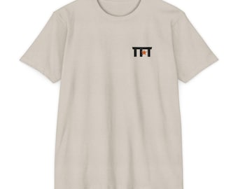 May include: A light beige short-sleeve t-shirt featuring a small black graphic on the upper left chest. The graphic consists of two vertical black bars connected by a horizontal bar, with a small orange star positioned in the center.