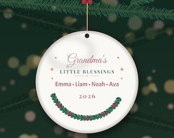 Op de afbeelding: Een rond wit keramieken ornament met de tekst Grandma's LITTLE BLESSINGS, de namen Emma, Liam, Noah en Ava, en het jaartal 2026. Het ontwerp bevat kleine gouden sterren en een groene hulstkrans met rode bessen aan de onderkant.