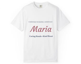 Op de afbeelding: Een wit t-shirt met korte mouwen voorzien van de tekst CERTIFIED NURSING ASSISTANT in donkerblauw, de naam Maria in een groot roze cursief lettertype en de tekst Caring Hands • Kind Heart in donkerblauw gecentreerd op de borst.