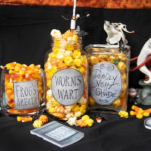 May include: Halloween-themed display featuring jars of popcorn and candy corn with labels that read "Frog's Breath", "Worm's Wart", and "Deadly Night Shade". Decorative figurines of characters from The Nightmare Before Christmas are also present.