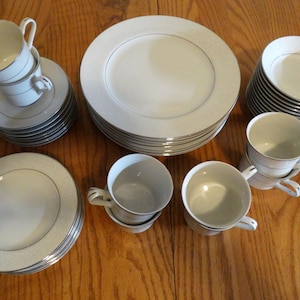 May include: A set of white porcelain dinnerware with a silver rim. The set includes plates, bowls, and cups.